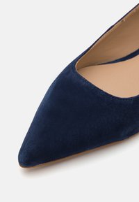 Sapatilha em camurça azul-marinho, de bico fino, com um corte baixo e um forro suave, apresentando um design elegante e minimalista.