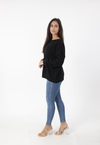 Czarny sweter dzianinowy o luźnym kroju, zestawiony z jasnoniebieskimi rurkami i przezroczystymi sandałami na słupku, podkreślający prosty, ale nowoczesny design.