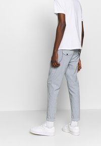 Striped pants in light blue and white fabric, tapered design, cuffed hems, with a back pocket and matching sneakers. Simple white t-shirt.