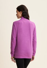Maglia a maniche lunghe viola con collo alto, struttura morbida e taglio dritto, con un orlo che si allunga leggermente sul retro.