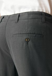 Pantalons en lin gris avec une poche arrière plate et une fermeture à un seul bouton. Le tissu a une finition texturée et la taille est dotée de passants de ceinture.