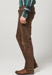 Jeans de mezclilla marrón con un corte recto, tejido texturizado y diseño de cinco bolsillos, combinados con botas de cuero marrón.