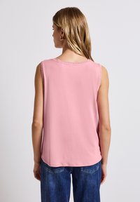 Hihaton vaaleanpunainen toppi, joka on valmistettu kevyestä kankaasta, jossa on pyöreä pääntie koristeompeleilla. Asua täydentää rento niiden denimfarkut.