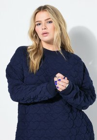 Marineblaues, gesteppte Sweatshirt mit Herzmuster, gerippten Bündchen und Rundhalsausschnitt. Weiche Textur, lockerer Schnitt und lange Ärmel.