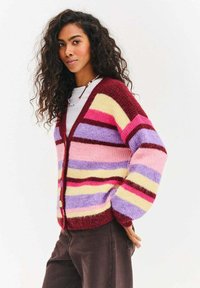 Prążkowany kardigan w kolorach bordowym, różowym, fioletowym i żółtym. Miękka, puszysta faktura, dekolt w serek, długie rękawy i zapięcia na guziki.