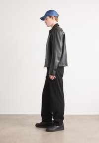 Black leather jacket, blue cap, black wide pants, black sneakers. The jacket has a smooth texture, with a simple design and no visible logos.