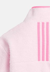 Veste en polaire rose clair avec un col haut et trois rayures verticales roses dans le dos, fabriquée dans un tissu doux et texturé.
