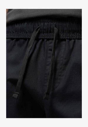 Black athletic shorts with a textured, lightweight fabric. Features an elastic waistband with a drawstring adjustment and side pockets.