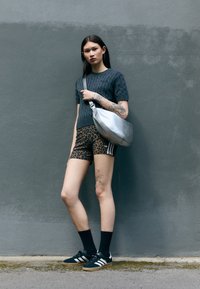 Pull à manches courtes en tricot gris, shorts imprimé léopard avec des rayures blanches, chaussettes noires et baskets en daim noires avec des accents blancs. Sac à épaule en argent.