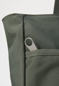 Grön tygväska med en texturerad yta, som har en liten ytterficka och en metallisk dragkedjepull med en rund öppning.