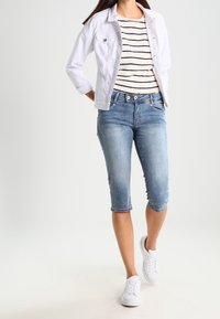 Chaqueta de mezclilla blanca, camiseta a rayas con cuello barco, vaqueros ajustados azul claro cortados a la altura de la rodilla y zapatillas blancas. Conjunto de ropa casual.