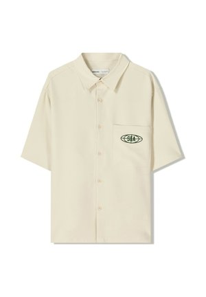 Camicia a maniche corte di colore beige con bottoni e colletto, caratterizzata da un logo verde sulla tasca sinistra del petto. Tessuto liscio e leggero.