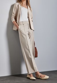 Béžové texturované sako přes bílý top, doplněné béžovými širokými kalhotami s předními záhyby. Světle barevné baleríny s pásky kolem kotníků.