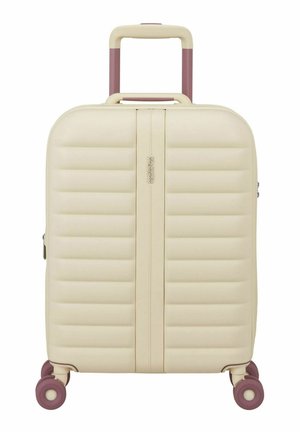 Maleta rígida beige con diseño acolchado vertical, asa retráctil y cuatro ruedas giratorias moradas, marca American Tourister.