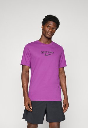Lilla Nike Pro T-shirt med rund halsudskæring og korte ærmer. Har et sort Nike-logo og tekst på forsiden. Materialet ser glat ud.