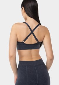 Sujeción deportiva de color gris oscuro con tirantes cruzados y herrajes ajustables. Fabricada con un material suave y un diseño sin costuras.
