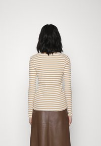 Langärmliges gestreiftes Oberteil in Creme und Beige, enganliegendes Design, gerippte Textur, mit rundem Ausschnitt. Kombiniert mit einem Rock aus braunem Leder.