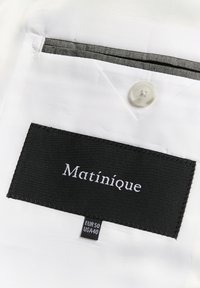 Valge kangas musta sildiga, millel on kirjas "Matinique". Sisaldab nuppu ja kontrastset halli taskukaunistust. Sisaldab suuruse silte.