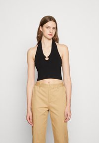 Top cropped preto com alças, textura canelada e um detalhe metálico circular na gola, combinado com calças de cintura alta bege.