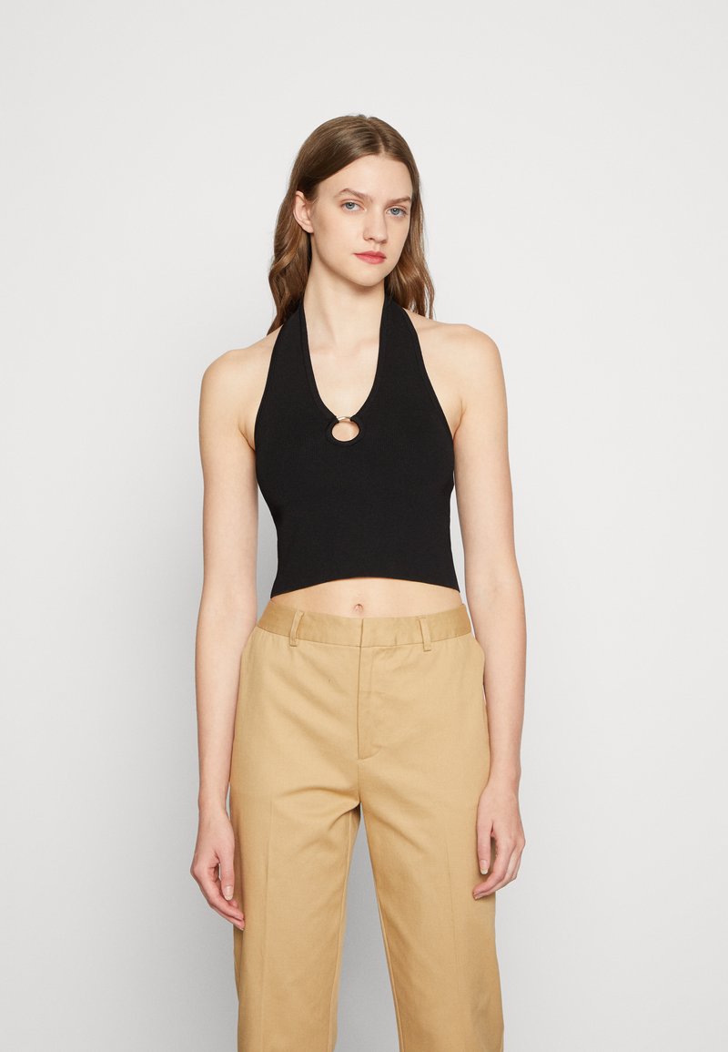 Top cropped preto com alças, textura canelada e um detalhe metálico circular na gola, combinado com calças de cintura alta bege.