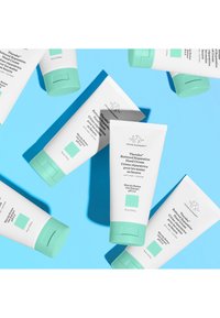 Drunk Elephant hand cream tubes with white bodies, mint green caps, and a teal square label, arranged on a bright blue background.