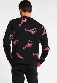Sudadera negra con un patrón de jirafas rosas repetido. El diseño tiene un escote redondo y puños y dobladillo acanalados. Textura suave.