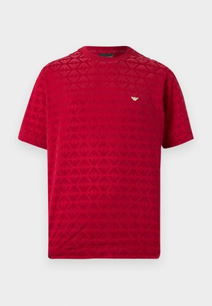 Červené tričko s krátkými rukávy, zdobené texturovaným vzorem a malým zlatým logem na hrudi. Hladká látka s kulatým výstřihem.