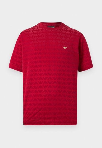 Rdeča majica s kratkimi rokavi z teksturiranim vzorcem in majhnim zlatim logotipom na prsih. Gladek material z okroglo izrezom na vratu.