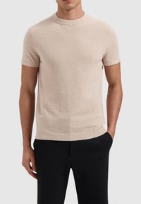 Beige short-sleeve sweater with a textured finish, round neckline, and ribbed cuffs and hem. Paired with black trousers.