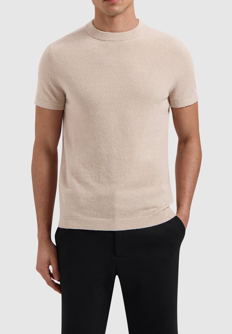 Beige short-sleeve sweater with a textured finish, round neckline, and ribbed cuffs and hem. Paired with black trousers.
