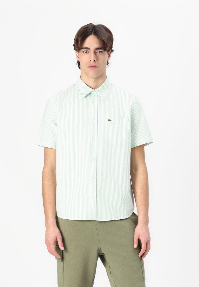 Maglietta a maniche corte, di colore verde chiaro a righe, con bottoni sul davanti, texture morbida e taschino sul petto discreto con logo del marchio.