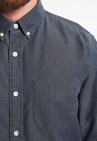 Chemise à manches longues gris foncé en coton avec une poche poitrine, des boutons de couleur plus claire et un col classique.