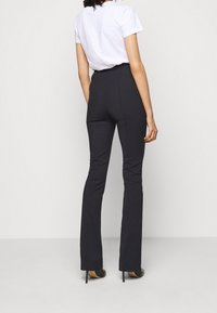 Pantaloni neri a palazzo su misura con vita alta e tasche posteriori, indossati con una t-shirt bianca a maniche corte e tacchi neri.