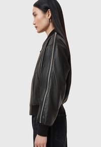 Giacca bomber in pelle nera con design cropped, polsini a coste, tasche laterali e dettagli con zip argentata lungo le maniche.
