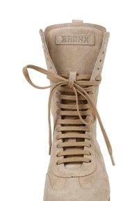 Bottine montante en daim beige avec des lacets beige noués en nœud et une étiquette « BRONX » sur la languette.