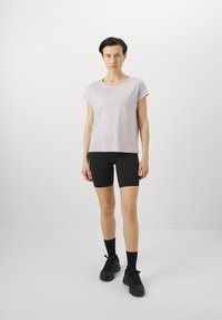 Lys lavendel kortermet t-skjorte kombinert med svarte tettsittende sykkelshorts. Modell iført svarte treningssko og knelange svarte sokker.