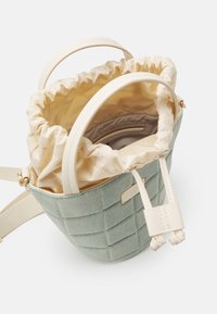 Okrągła torebka w stylu koszyka wykonana z teksturowanej, jasnozielonej tkaniny z kremową, satynową podszewką, posiadająca marszczony wierzch i regulowane paski.