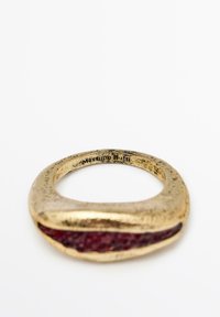 Anello in metallo dorato con superficie irregolare, caratterizzato da un interno liscio di colore rosso. Inciso con la scritta "Massimo Dutti" sulla fascia interna.