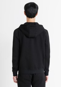 Sudadera con capucha negra hecha de una tela suave, con un corte relajado, puños y dobladillo de canalé. La capucha tiene un sutil detalle en la costura.