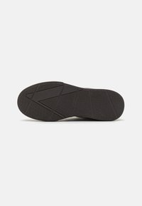 Black rubber shoe sole with textured surface, featuring a herringbone pattern and geometric grooves for traction and grip.