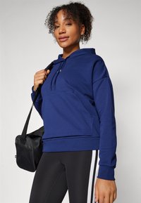 Sweatshirt azul-escuro com um bolso canguru, capuz com cordão e punhos canelados. Usado com leggings pretas que apresentam riscas brancas nas laterais.