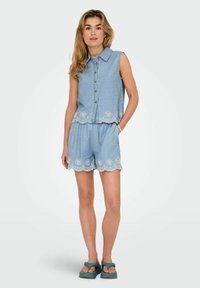 Svetlomodrý šambrejový dvojdielny outfit, ktorý sa skladá z bezrukávovej košele na gombíky a zodpovedajúcich šortiek. Ozdobný lem so zaobleným okrajom a dekoračným výšivkovým vzorom.