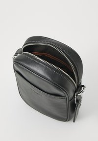 Borsa a tracolla in pelle nera con chiusura a zip, bordi arrotondati e tasca frontale. Presenta dettagli in metallo argentato e cuciture a contrasto.