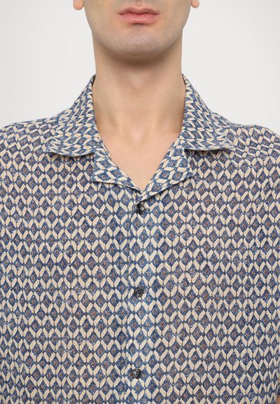 Krátky rukáv košele z ľahkej látky so svetlomodrým a béžovým geometrickým diamantovým vzorom. Má rozšírený golier a zapínanie na gombíky.