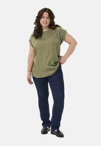 Bluză verde măsliniu, cu mâneci scurte și o croială lejeră, completată cu blugi negri. Partea de sus are un tiv rotunjit și o textură moale.