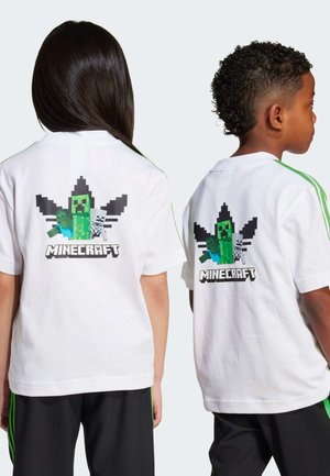 Weißes T-Shirt mit einem pixelierten Minecraft-Creeper-Graphic auf dem Rücken, umgeben von schwarzen Formen, dazu schwarze Hosen und grüne Akzente.