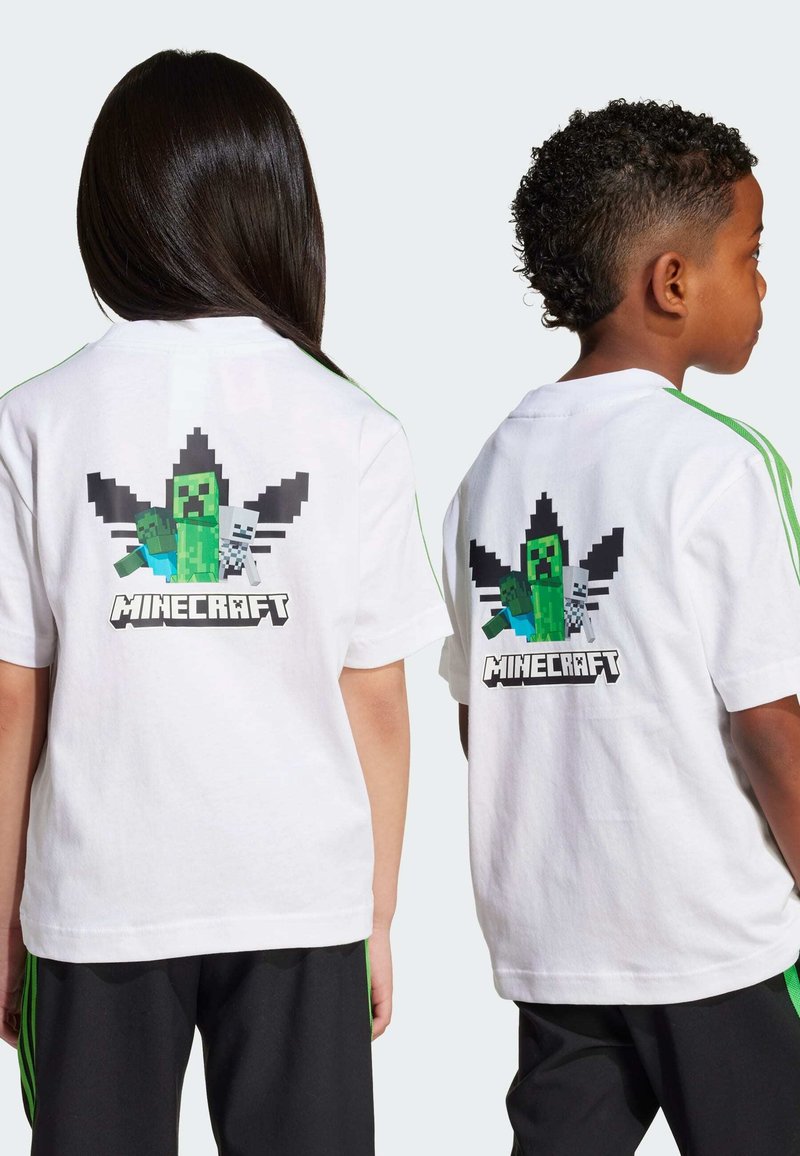 Biała koszulka z pikselowym nadrukiem stwora Creeper z gry Minecraft na plecach, otoczonym czarnymi kształtami, w połączeniu z czarnymi spodniami i zielonymi akcentami.