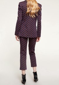 Navy kostymset med ett geometriskt mönster i orange. Blazer med långa ärmar och skräddarsydd passform; smala byxor med kortade benslut. Svarta ankelskor.