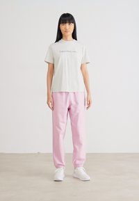 Grijze katoenen t-shirt met 'Calvin Klein Jeans' logo, gecombineerd met lichte roze joggingbroek en witte sneakers, gladde stof en eenvoudig ontwerp.