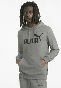 Sudadera gris hecha de un tejido suave que cuenta con un bolsillo tipo canguro, puños acanalados y un gran logo negro de Puma en el frente.